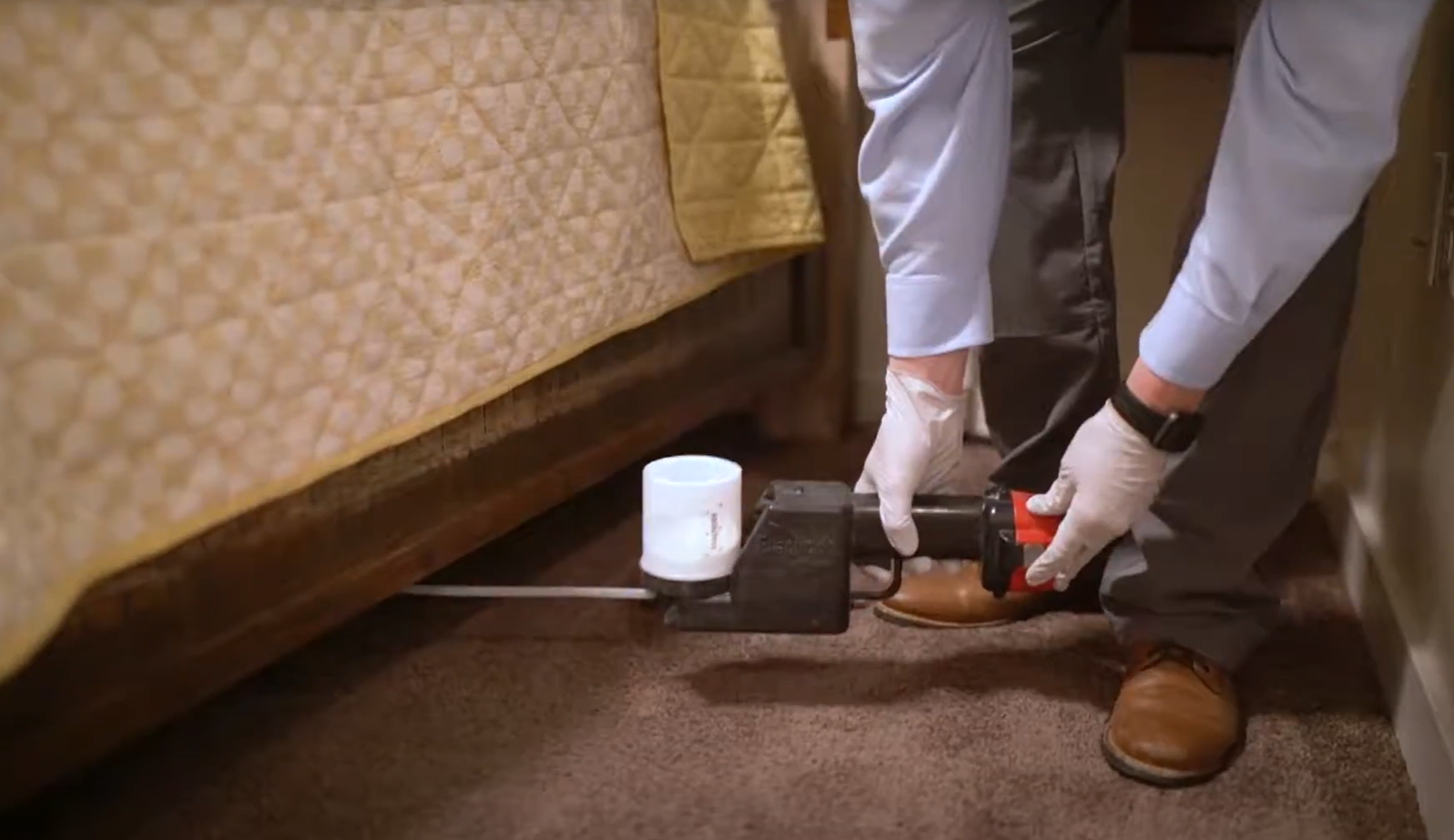 A pest control professional inspecting under a bed with specialized equipment during a pest control service in Council Bluffs.
