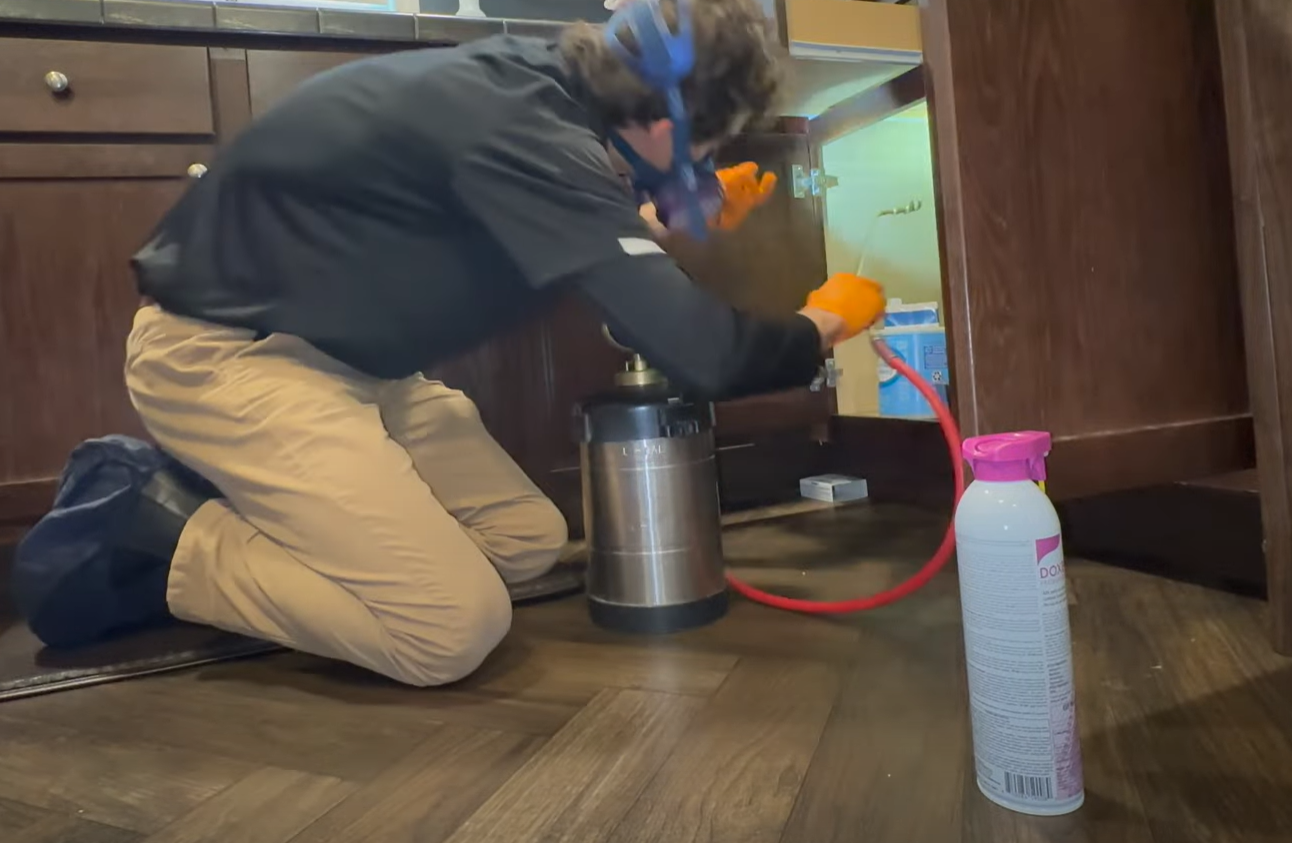 A pest control technician spraying inside kitchen cabinets to eliminate bugs during a pest control service in Council Bluffs.